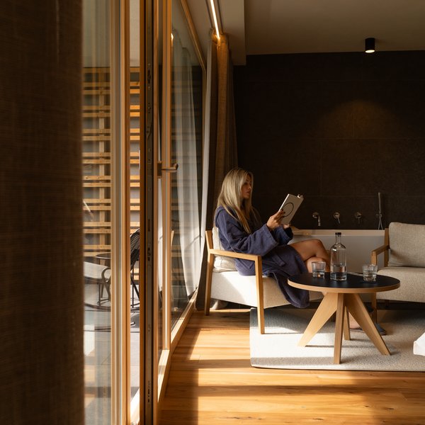 Your hotel in the Dolomites: Sensoria Dolomites Woman in bathrobe relaxing in modern living room reading a book