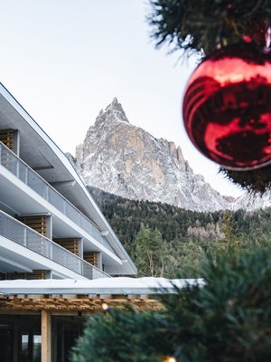 Sensoria Dolomites: Wellnesshotel in den Dolomiten Schneebedeckter Berg mit moderne Gebäude und roter Weihnachtskugel im Vordergrund