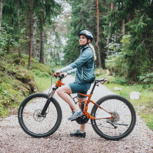 Your hotel in the Dolomites: Sensoria Dolomites Woman wearing helmet on orange mountain bike on forest trail